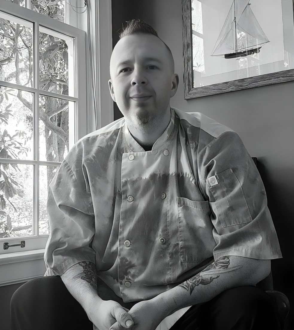 Chef Phil Charron in chef whites, seated by a window